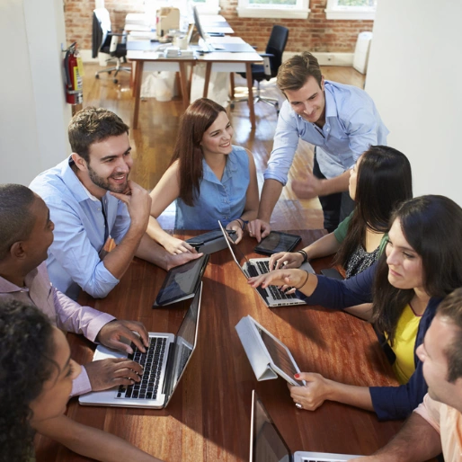 A group of individuals engaged in digital marketing training, seated around a table with laptops.